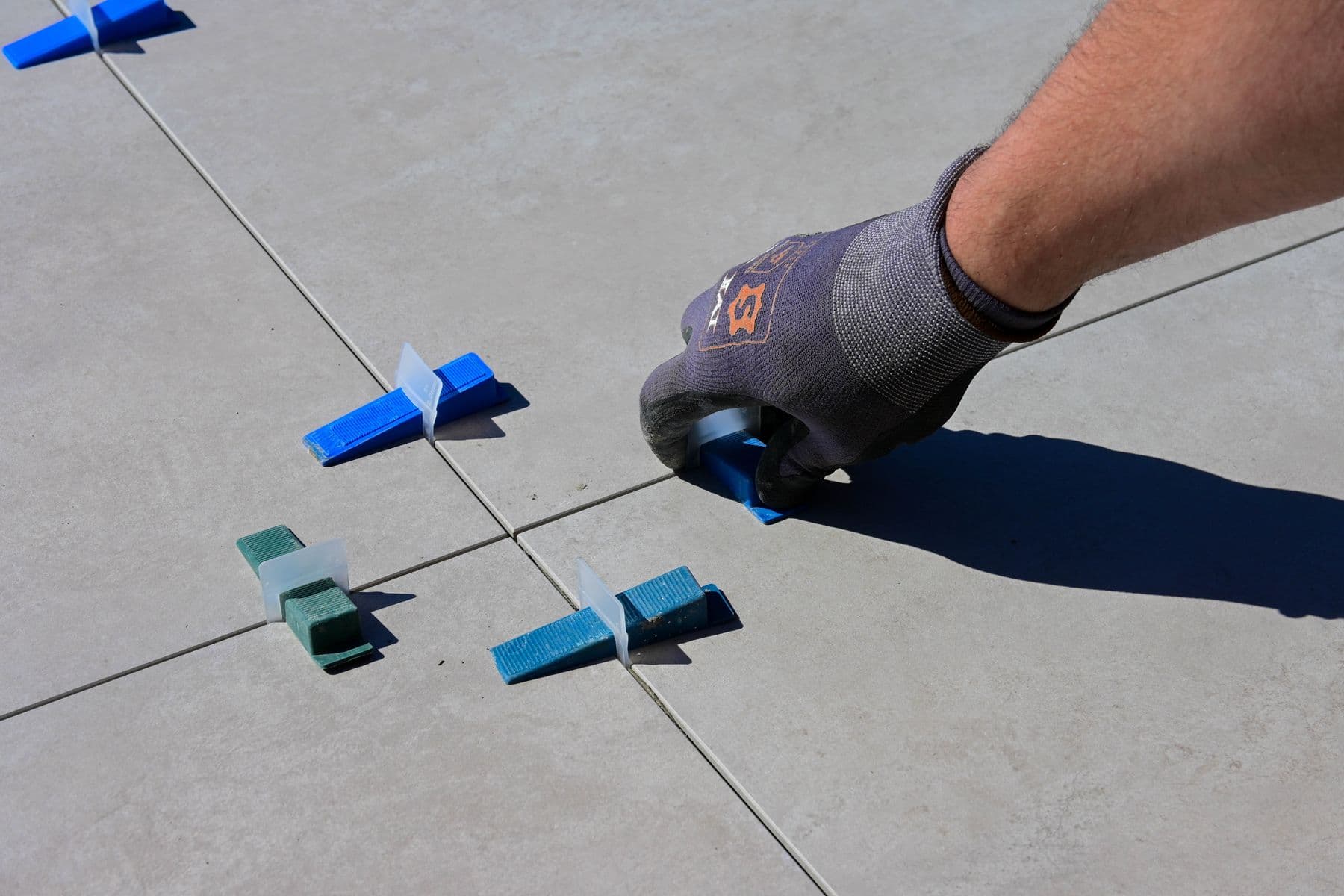 Gloved hand setting large-format porcelain floor tiles with leveling wedges